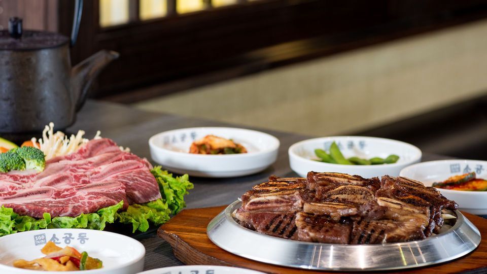 Tabletop with raw and grilled meat platters, side dishes, and greens in a restaurant setting