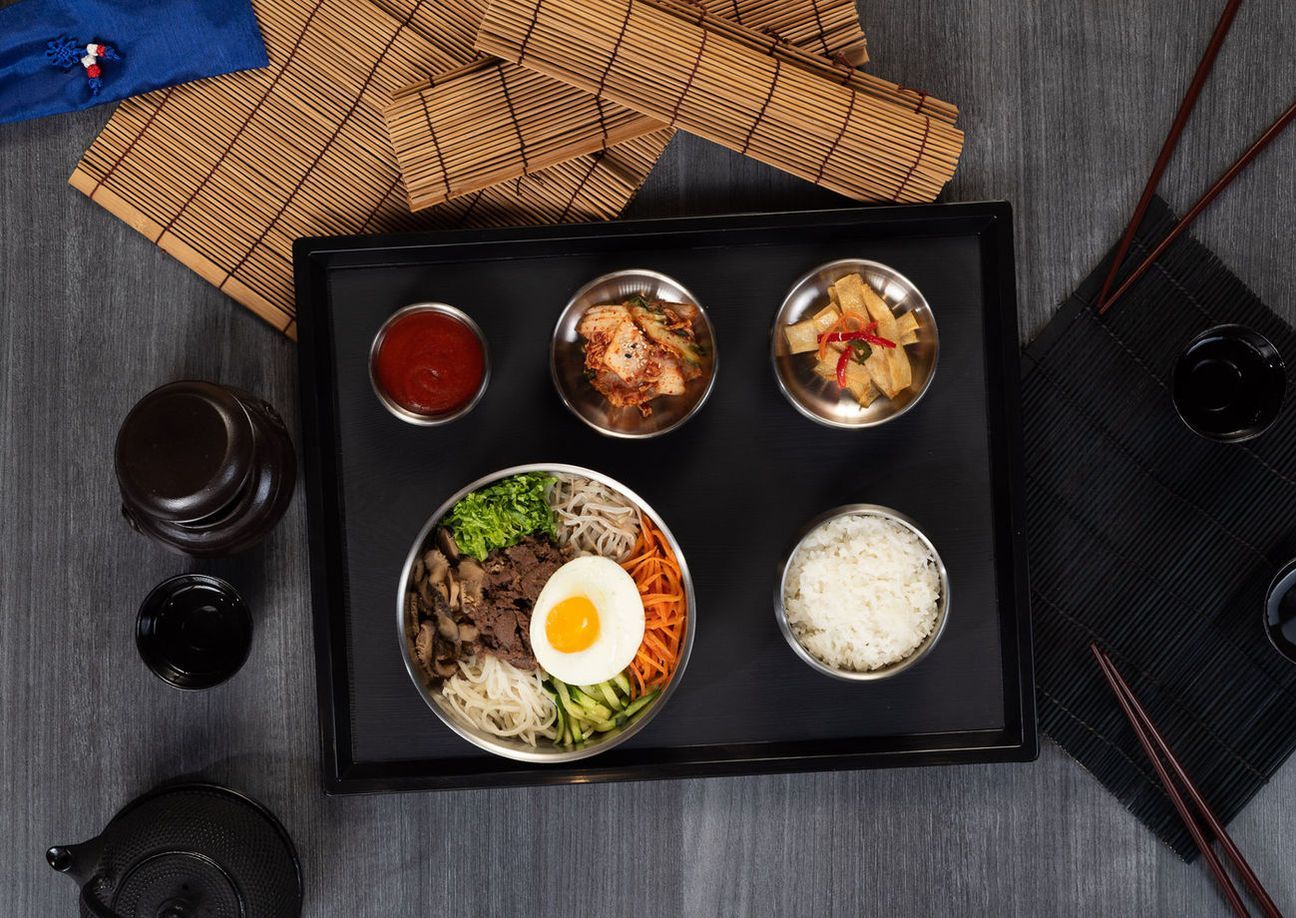 Japanese meal set on black tray with rice, soup, side dishes, and a bowl topped with an egg and greens
