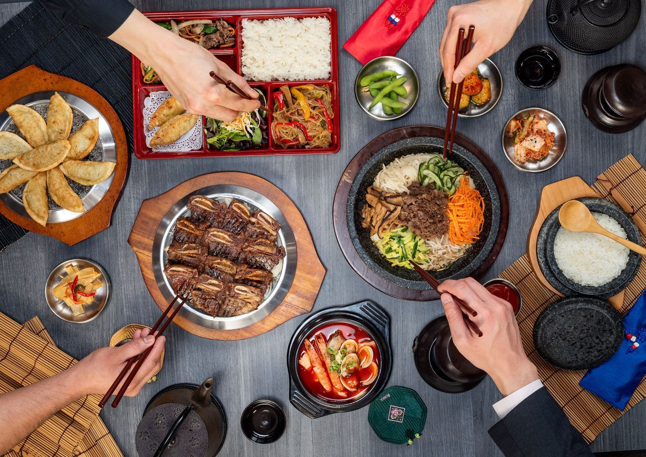Top-down view of a shared Japanese meal with sushi, rice, soup, and hands using chopsticks around a table