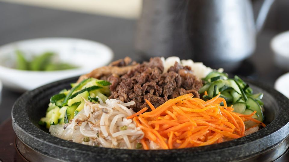 Bowl of bibimbap with beef, vegetables, and rice in a black stone bowl
