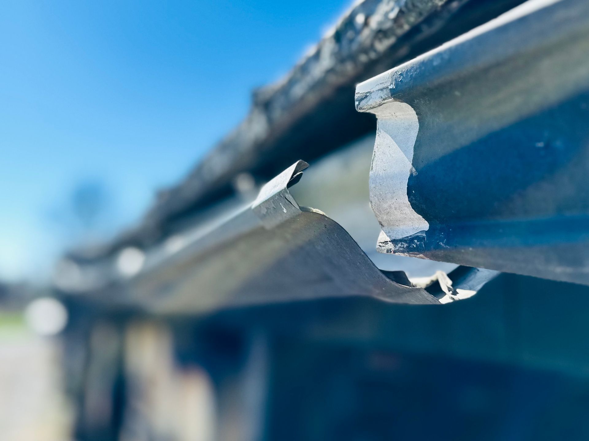 Damaged metal rain gutter on a roof, with chipped paint, against a blue sky.