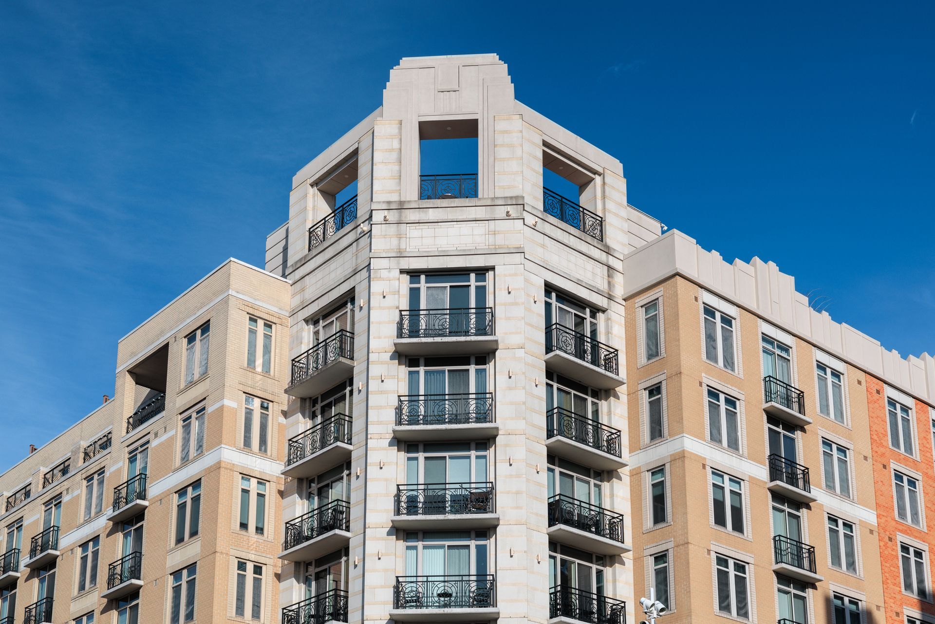 Multi-story tan and white building with balconies against a blue sky.