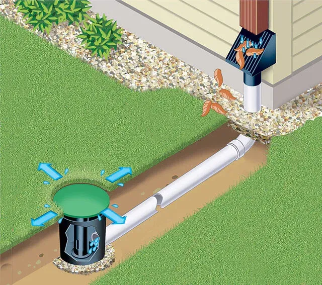 Black downspout draining onto rocks beside a building with concrete edging.