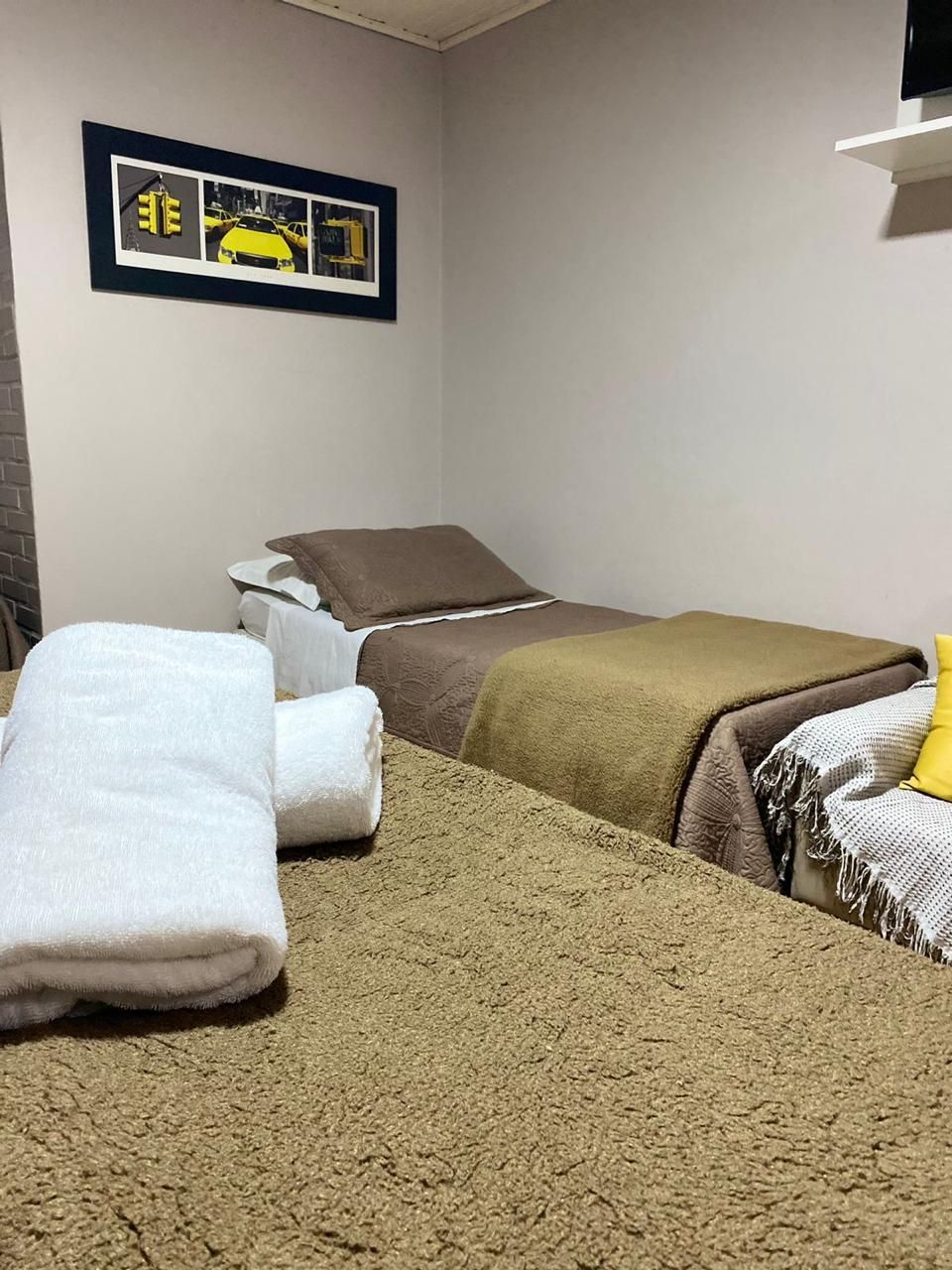 Duas camas com cobertores marrons, toalhas brancas, um quadro e paredes em tons neutros.