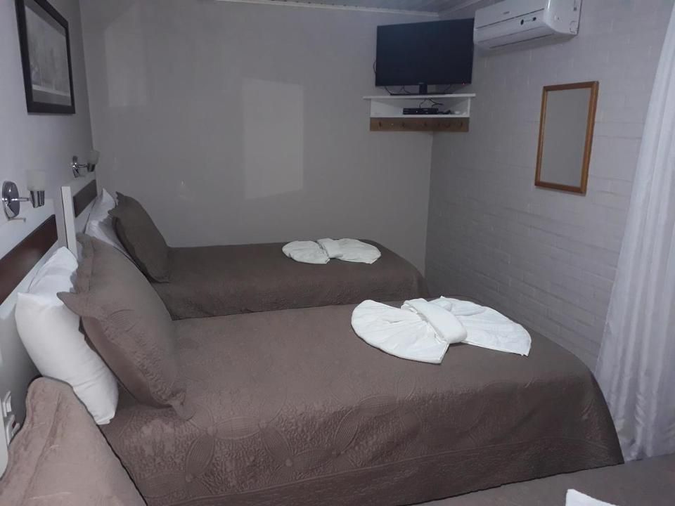Quarto de hotel com três camas de solteiro cobertas com lençóis marrons e toalhas dobradas por cima.