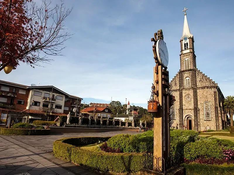 Torre do relógio em frente a uma igreja de pedra e edifícios em Gramado, Brasil, com céu azul.