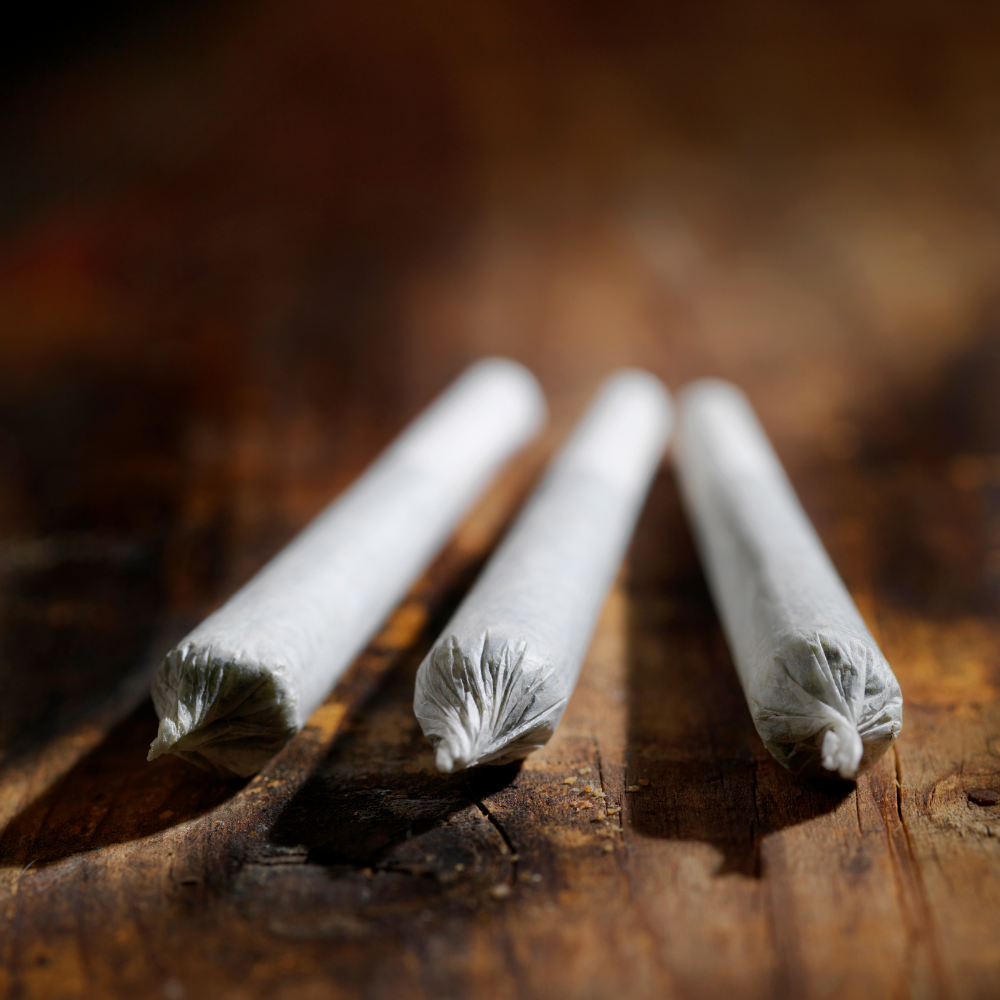 Three rolled cigarettes, with paper tips, lie on a wooden surface.