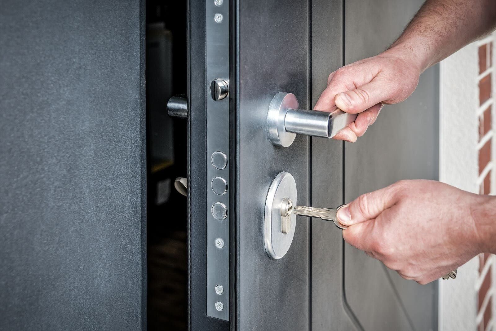 A person inserting a key into a metallic gray door lock while holding the door handle.