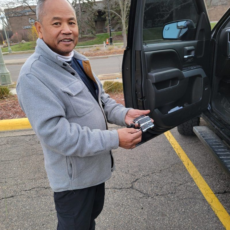 A person standing by an open car door in a parking lot, holding a small metal hardware piece in their hands.