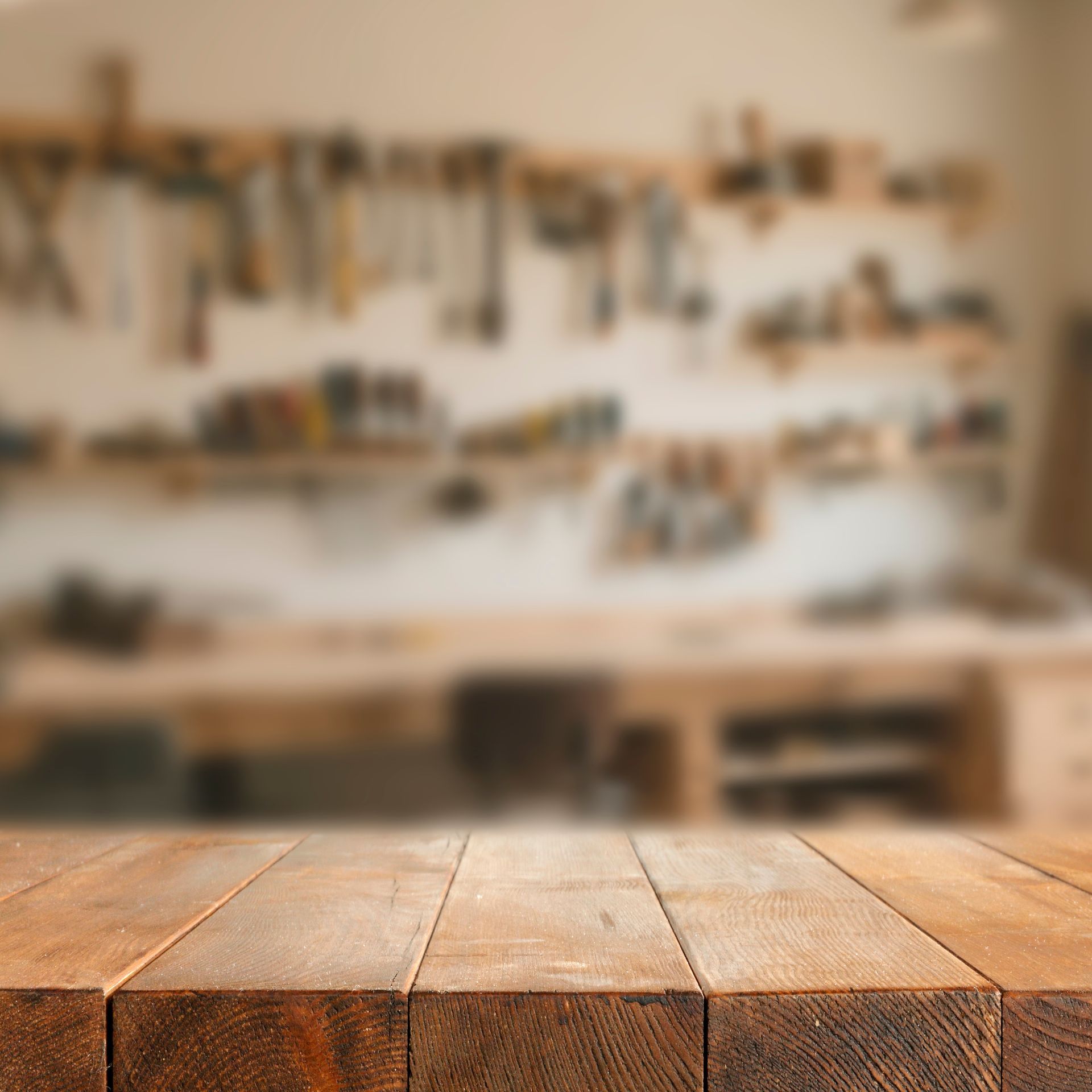 Wooden tabletop in front of a blurred workshop wall with hanging tools and shelves