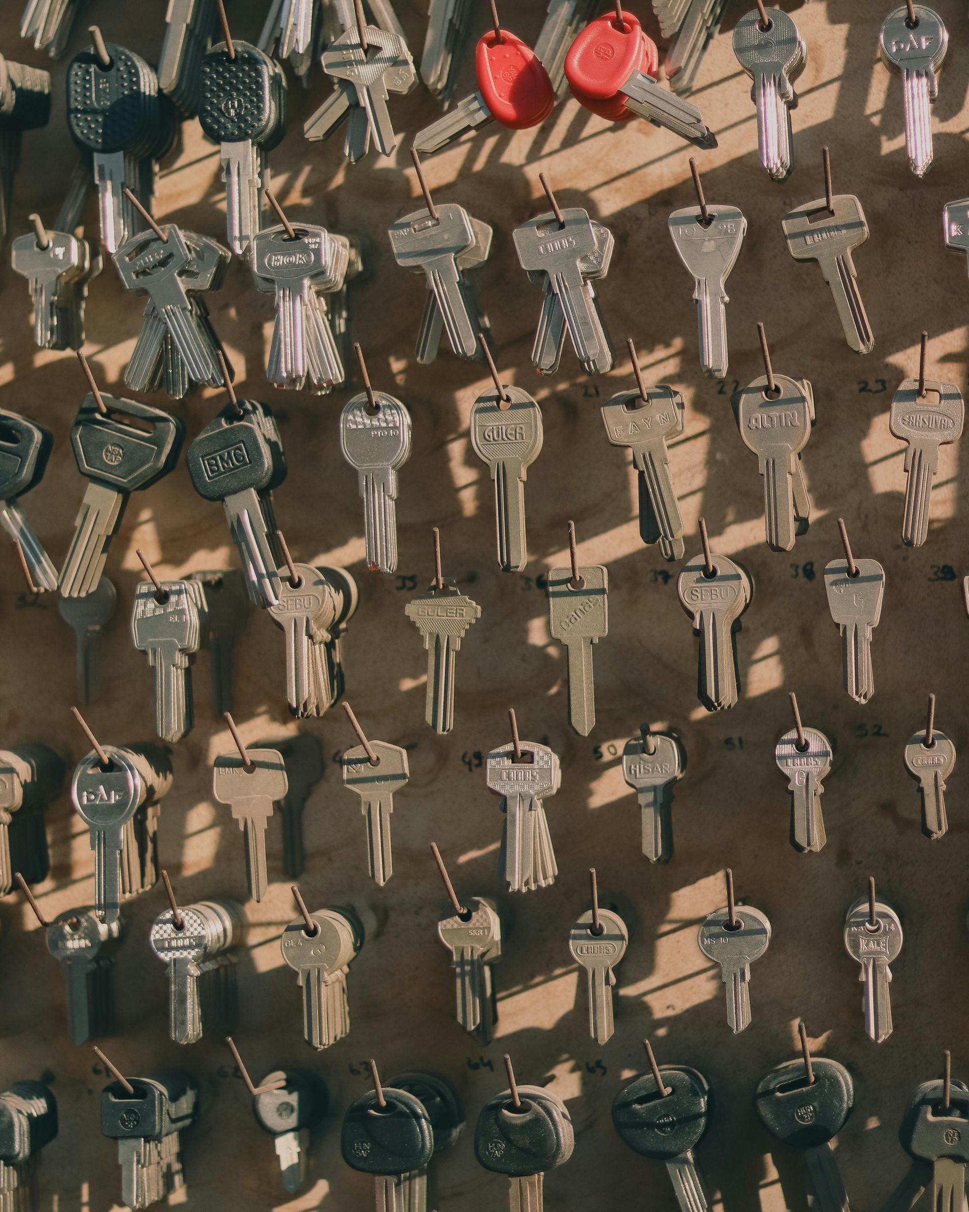 Many assorted keys hanging on a display board, with several red key covers near the top.