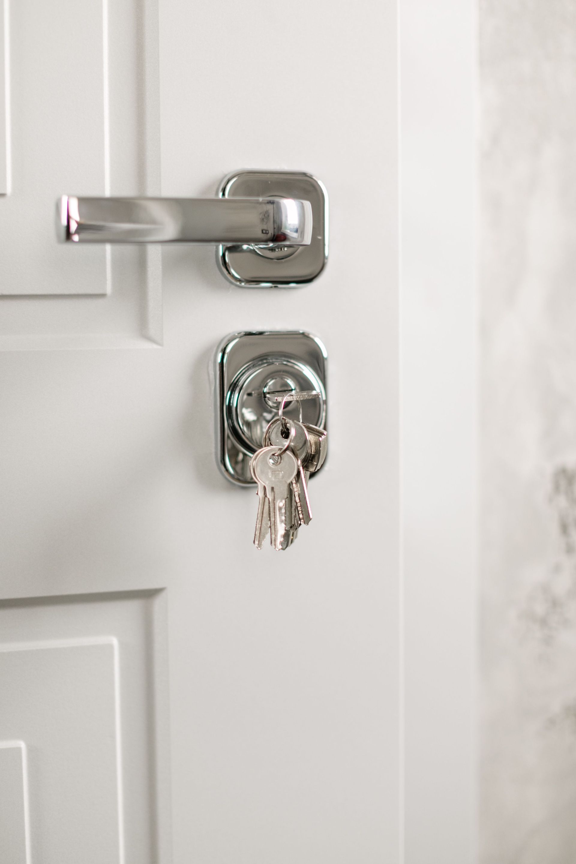 Close-up of a white door with a chrome deadbolt and a key inserted in the lock.