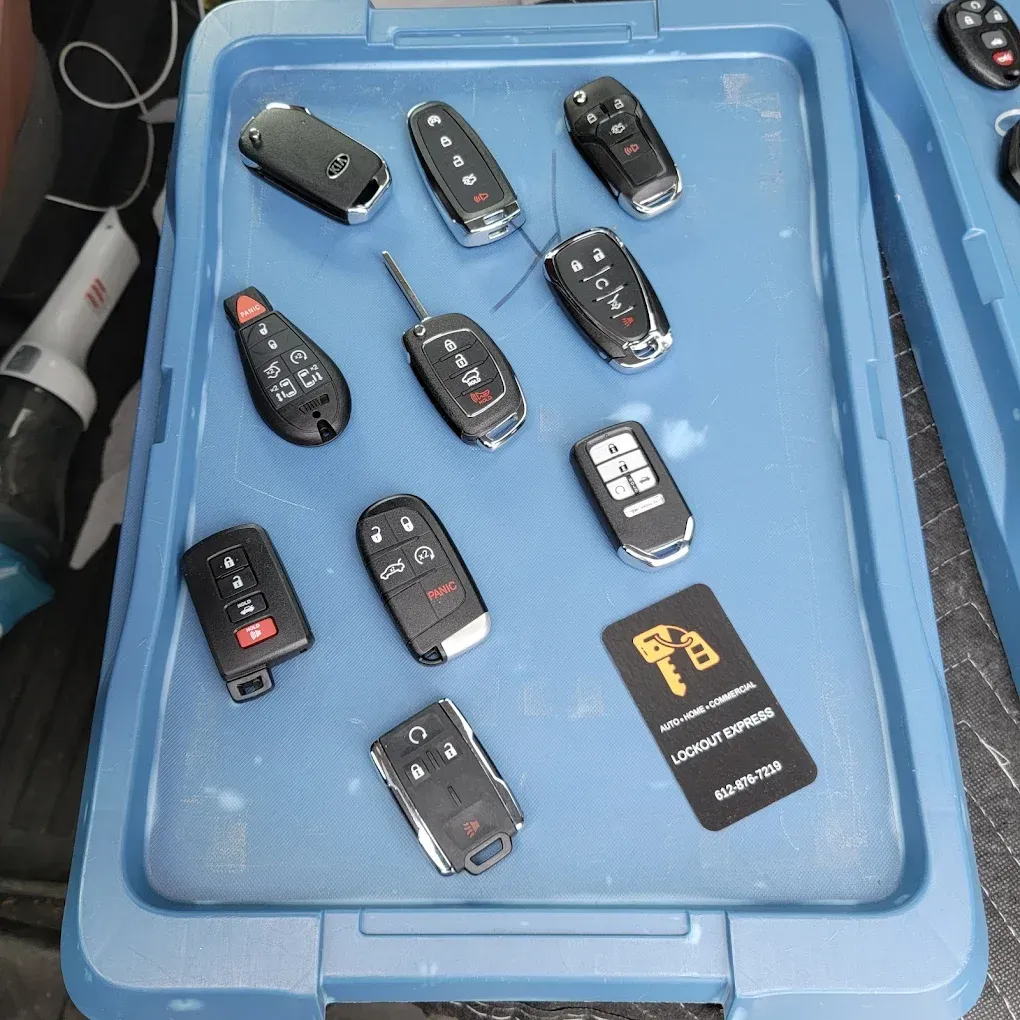 A blue plastic bin containing several assorted car key fobs and a black business card with a locksmith logo.