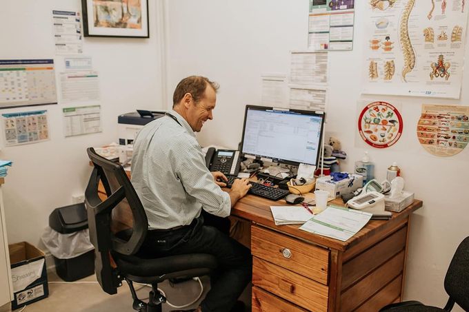 A Doctor Is Sitting at A Desk in Front of A Computer — Rural Medical Clinic In Manilla, NSW