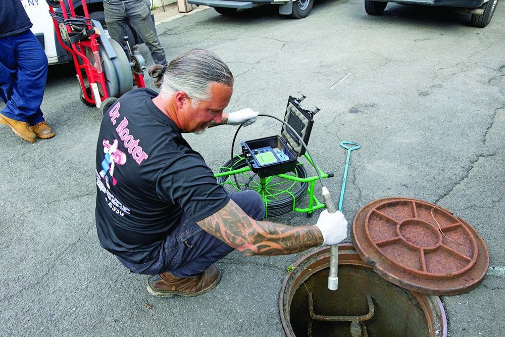 Man with tattoos inspecting a sewer with a camera on a sunny day.