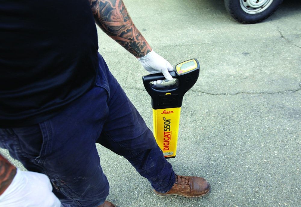 Person using a yellow and black cable locator on pavement, checking for underground utilities.