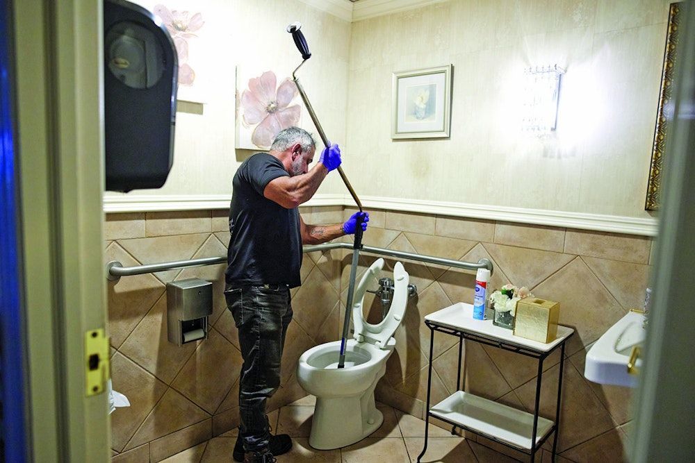 A man unclogs a toilet with a plunger in a public restroom.