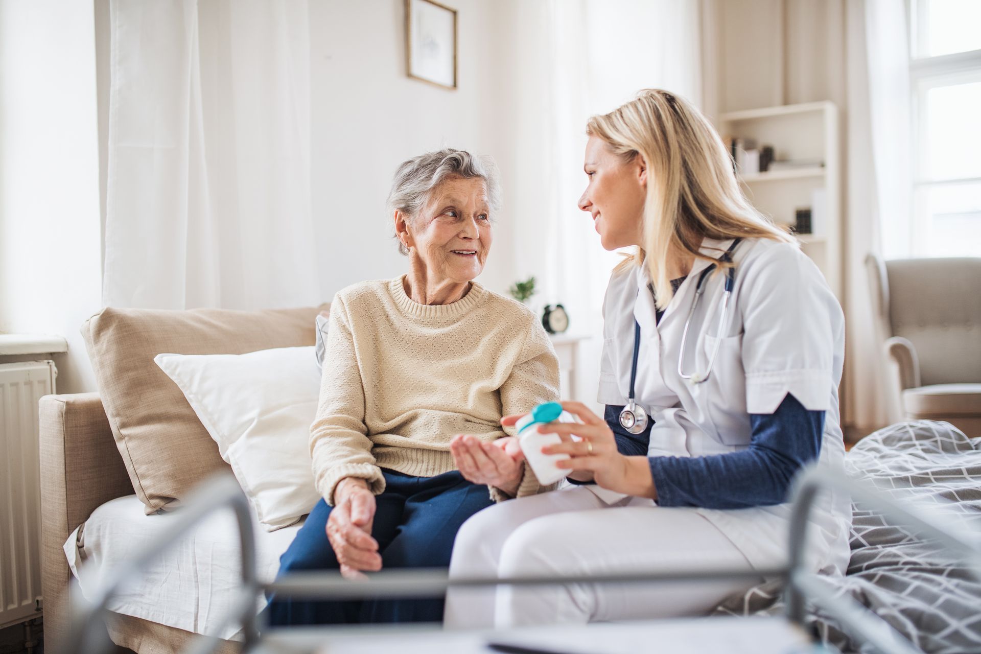 A nurse is giving an elderly woman a pill while sitting on a couch.