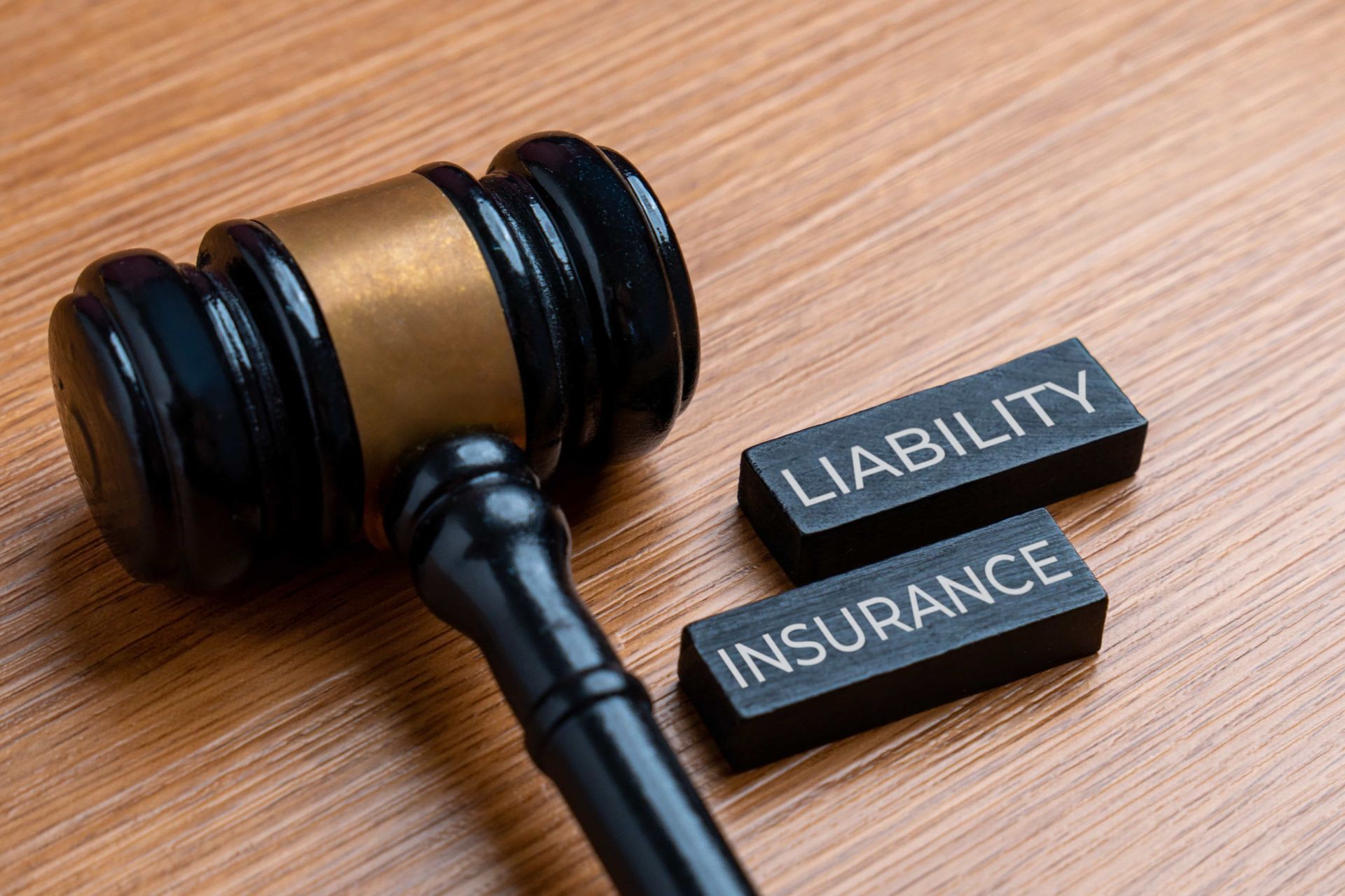 Judge’s gavel beside blocks labeled “LIABILITY” and “INSURANCE” on a wooden table