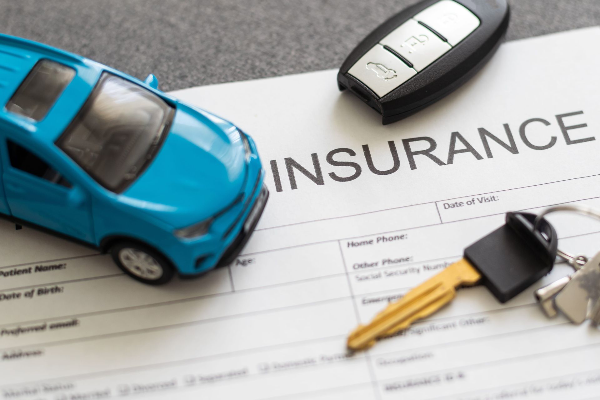 Blue toy car with keys on an insurance document, symbolizing auto insurance.
