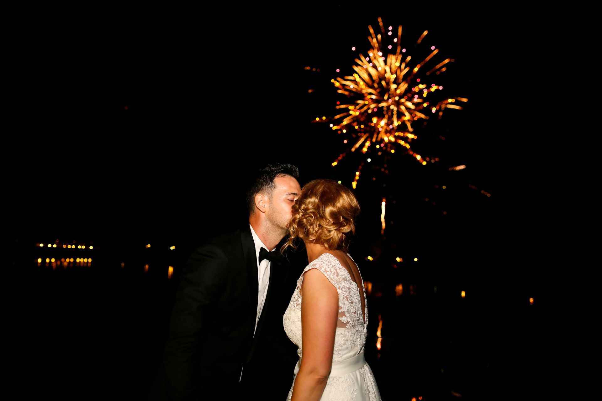 A bride and groom kissing in front of a fireworks display.