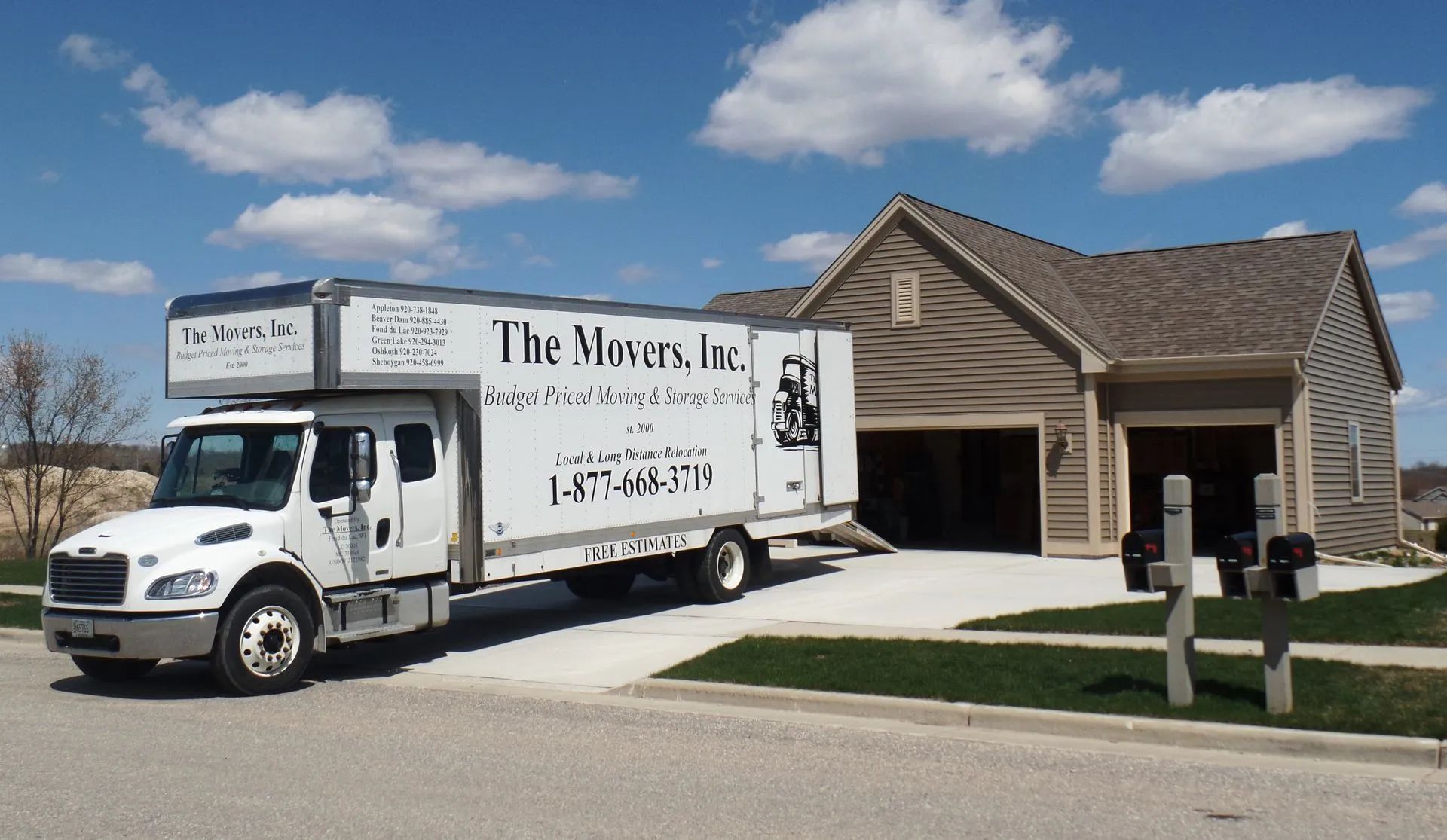White moving truck parked beside a tan house under a blue sky with clouds