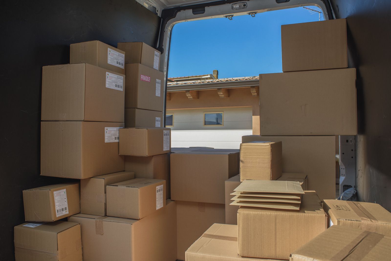 Packed cardboard boxes stacked inside a delivery van with a blue sky visible through the open rear door