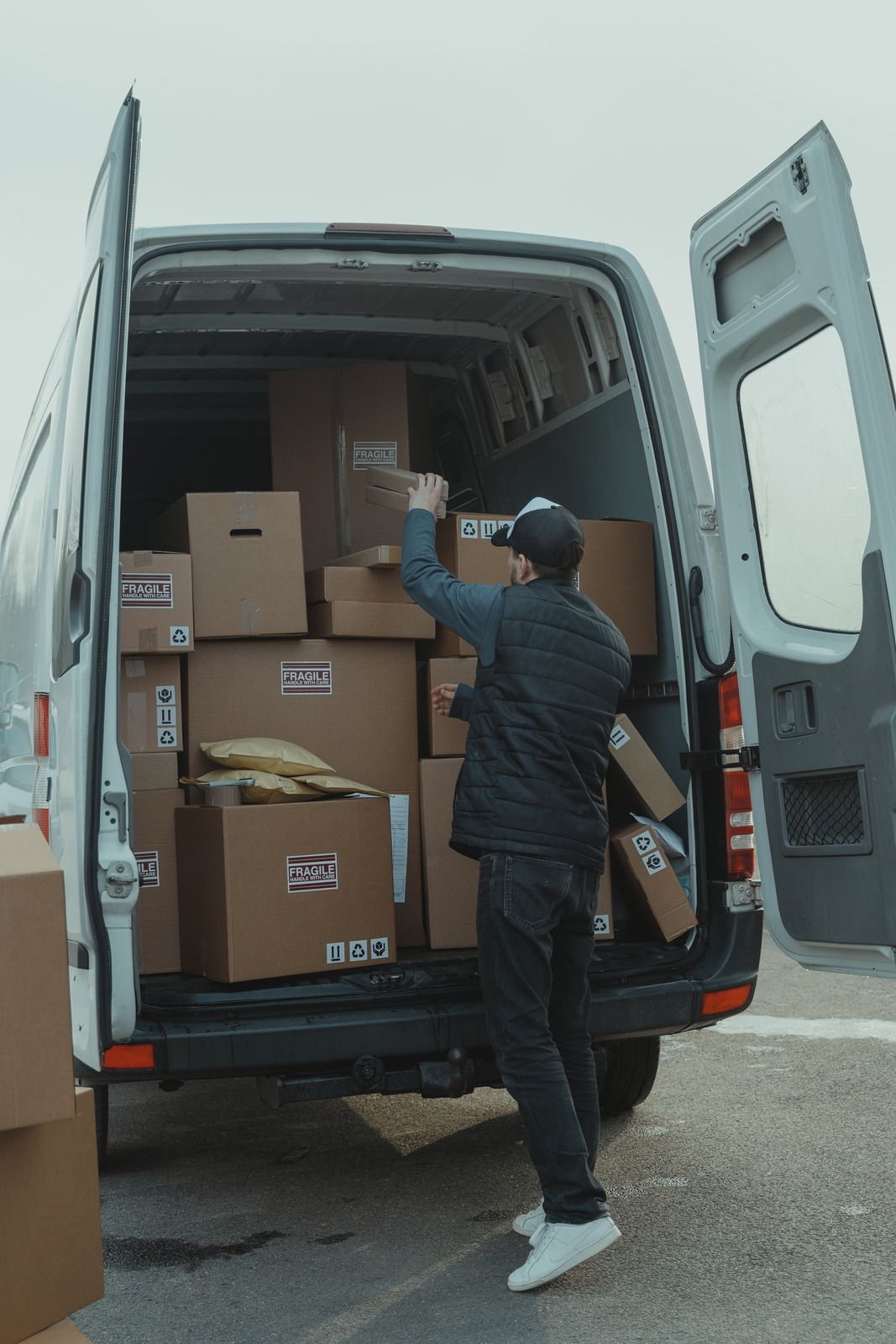 Delivery worker loading cardboard boxes into a van with open rear doors