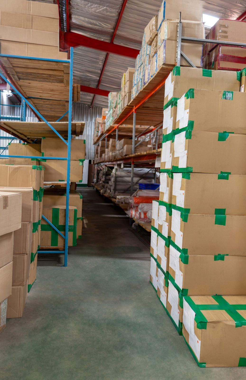 Warehouse aisle with stacked cardboard boxes on tall metal shelves and a clear walkway