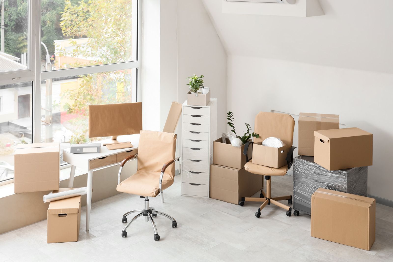 Bright home office with cardboard moving boxes, desk, chair, and sunlight by a window
