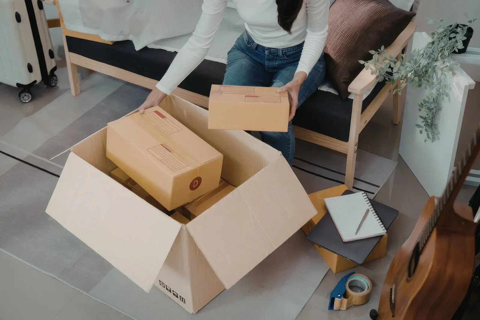 Person packing cardboard boxes in a living room with a couch and scattered moving supplies.