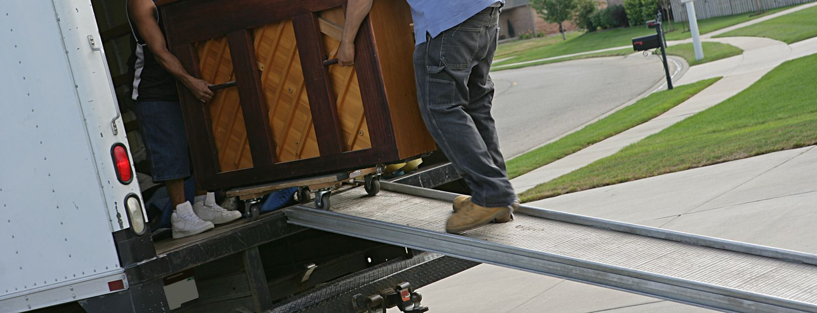 Person loading a large wooden item from a truck onto a ramp on a suburban street