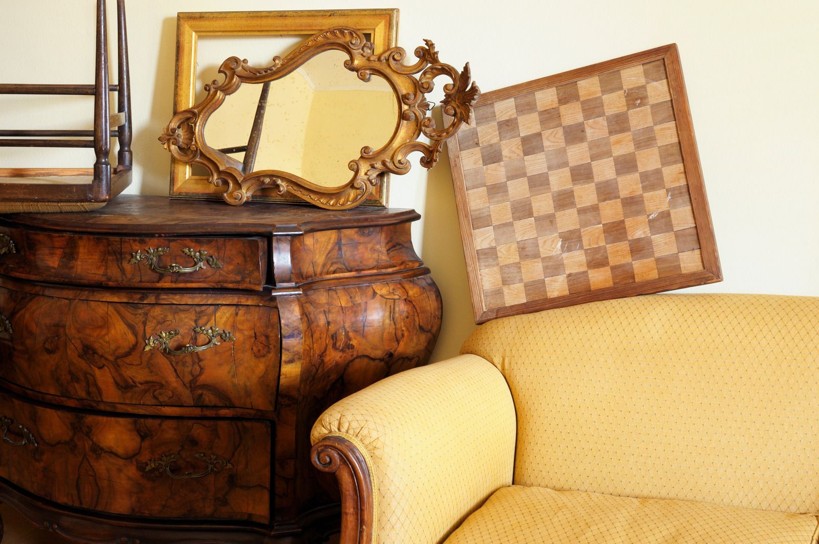 Ornate wooden dresser with mirror beside a yellow armchair and checkered wall art