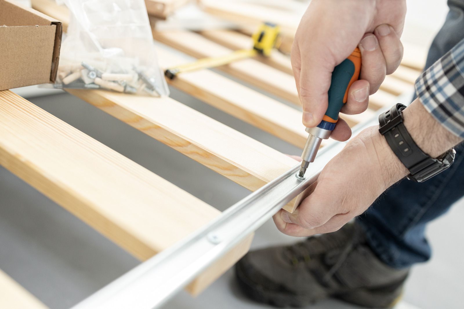 Hands measuring a wooden board with a tape measure and screwdriver during furniture assembly
