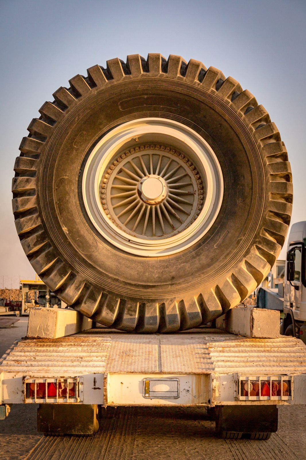 Massive off-road truck tire mounted upright on a flatbed truck at sunset