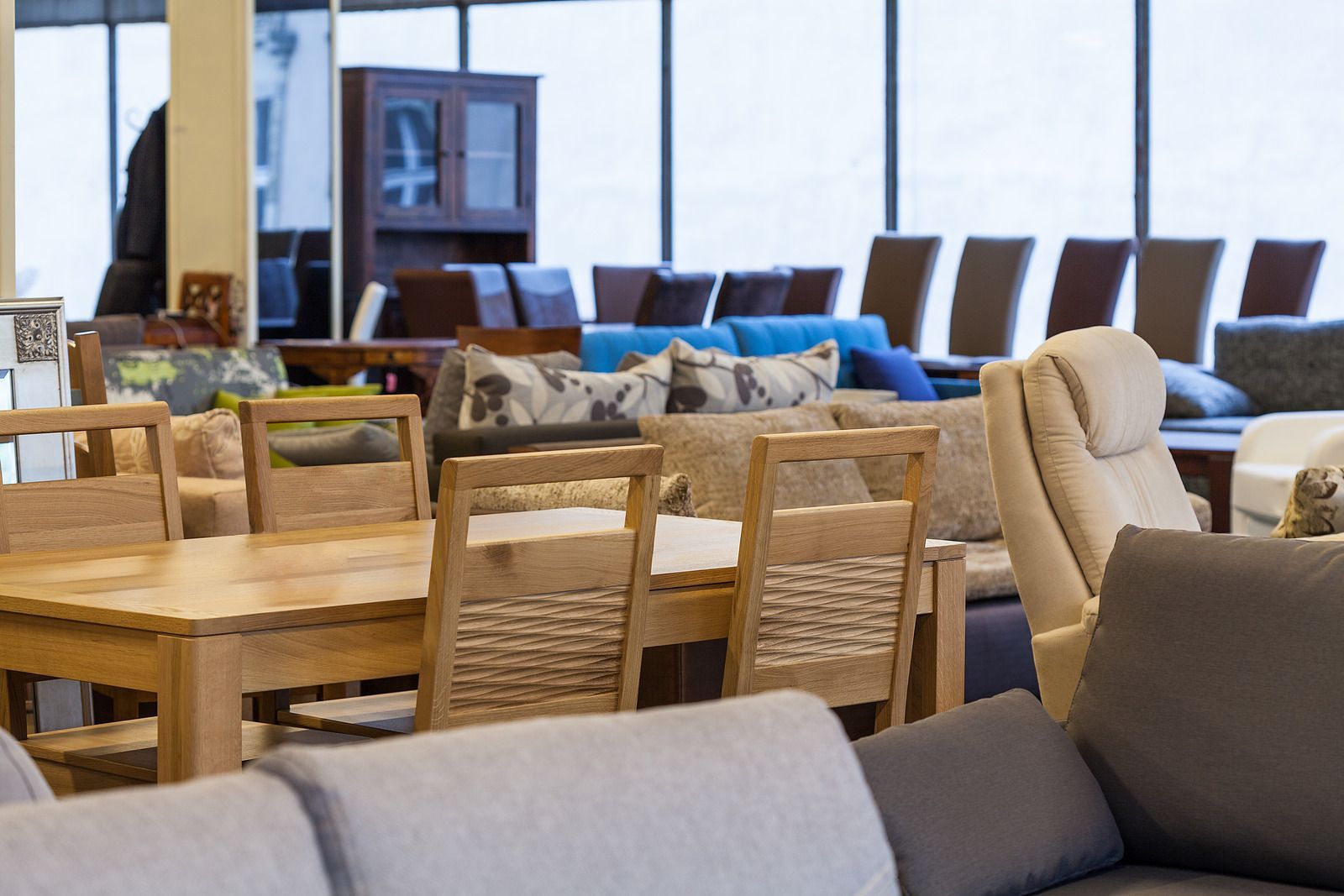 Furniture showroom with wooden tables and chairs, sofas, and lounge seating arranged in a bright display area