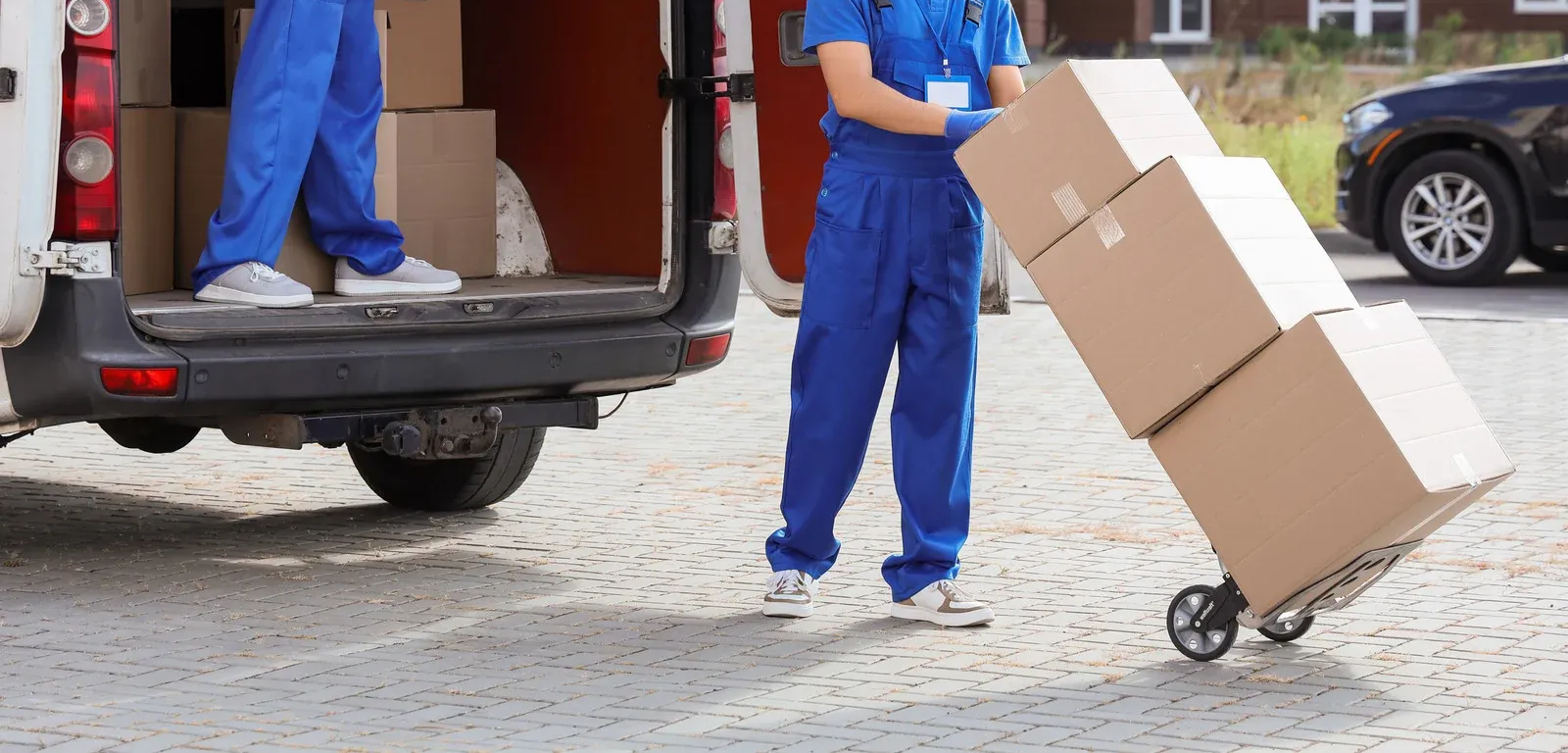 Mover in blue pants wheeling stacked cardboard boxes from a van