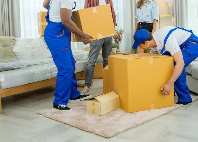 Three movers in blue uniforms packing large cardboard boxes in a living room