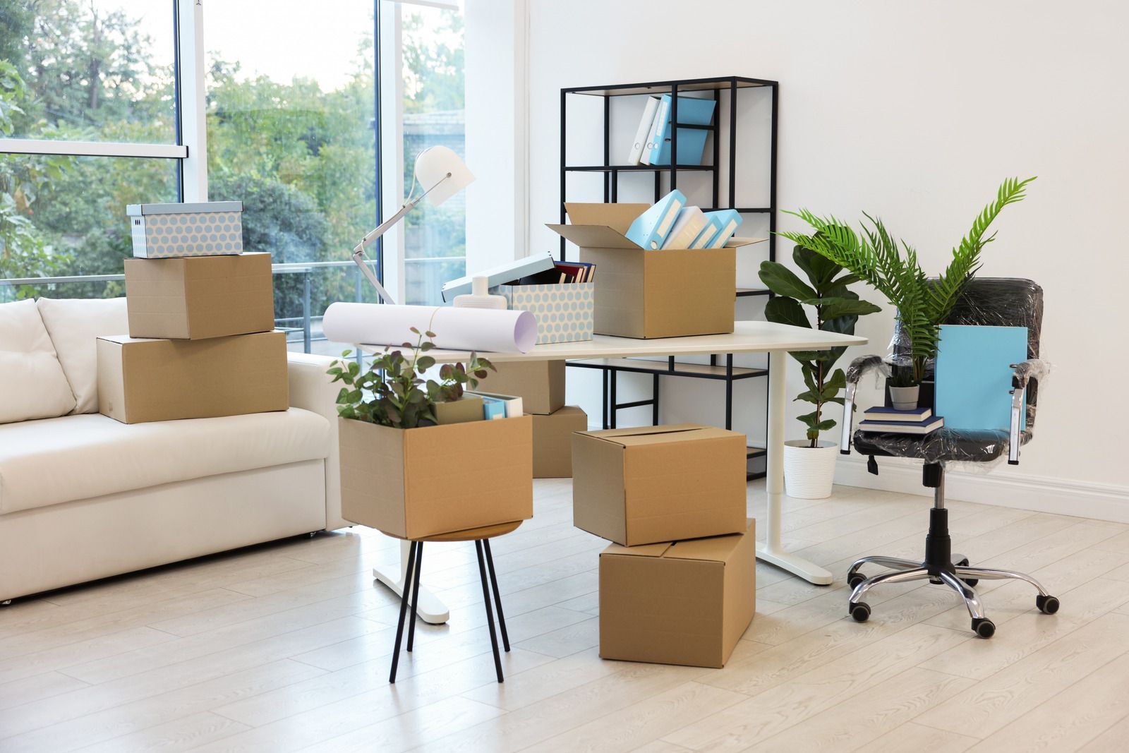 Bright home office with stacked moving boxes, desk, office chair, couch, and large windows