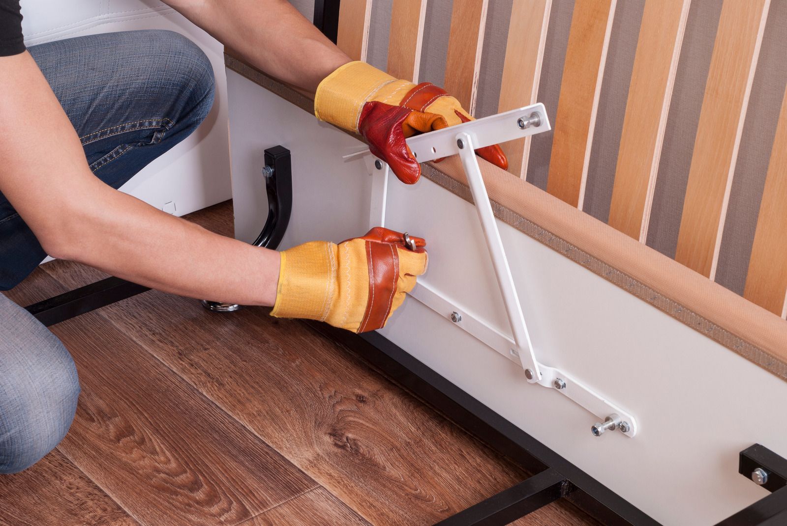 Person in yellow gloves assembling a white foldable table beside a striped wall