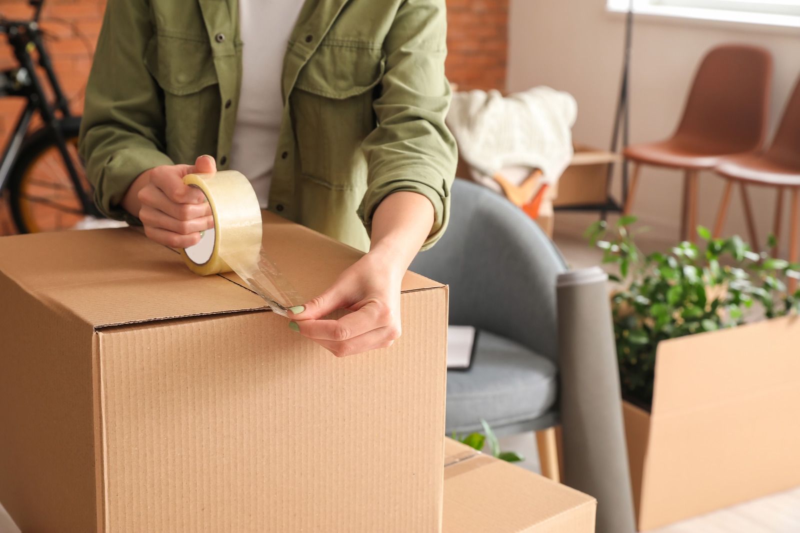 Person sealing a cardboard box with packing tape in a moving room