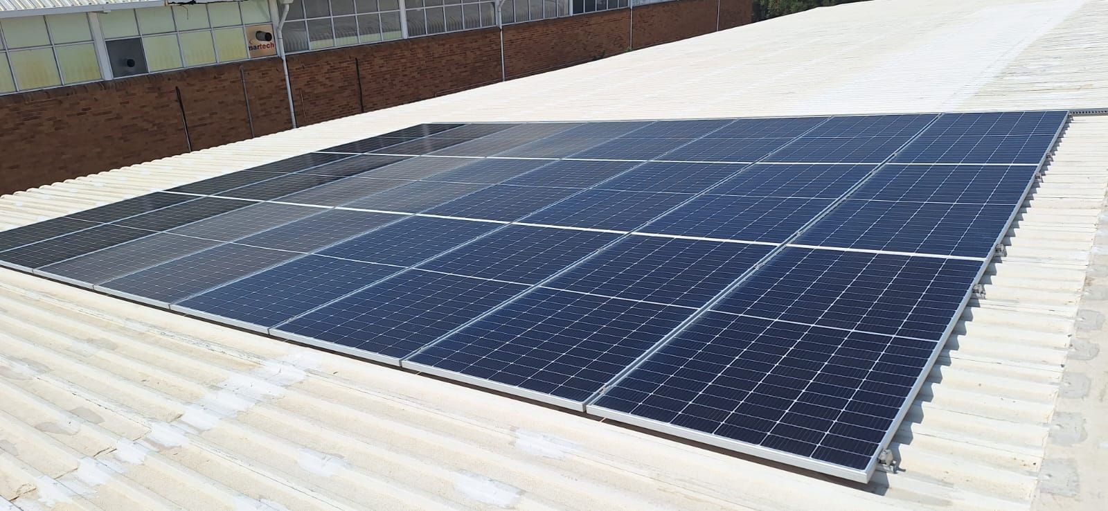 A grid of dark rectangular solar panels installed on a white corrugated metal roof.