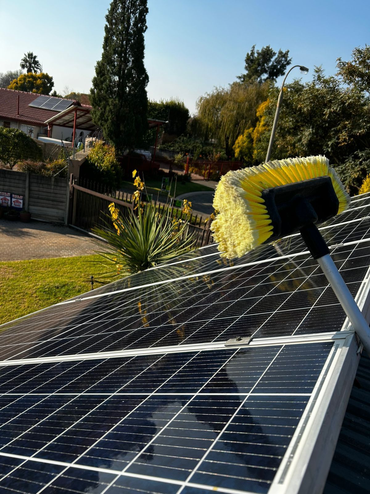 A yellow-bristled brush cleans dark solar panels on a rooftop during a sunny day.