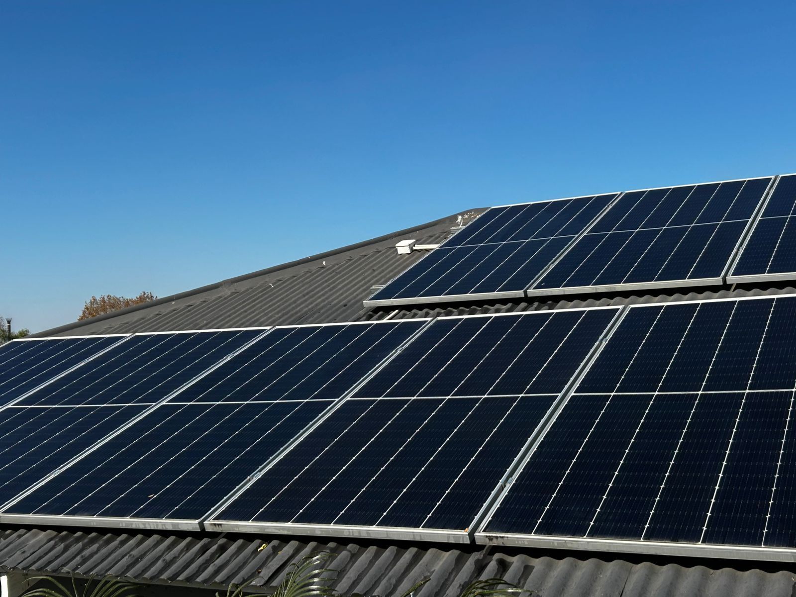 Black solar panels installed on a dark-tiled residential roof under a clear blue sky.