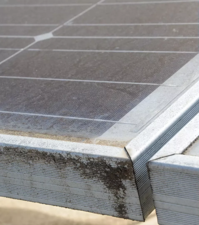 A close-up of the metal frames and glass surfaces of two adjacent solar panels, showing signs of dirt and weathering.