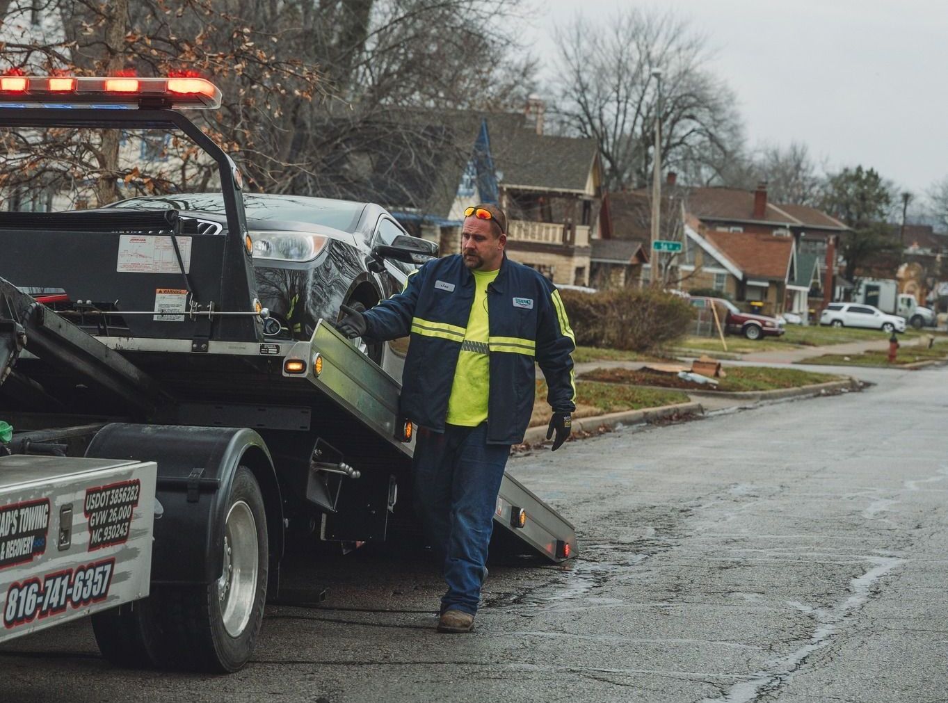 A man in a yellow shirt is standing next to a tow truck.
