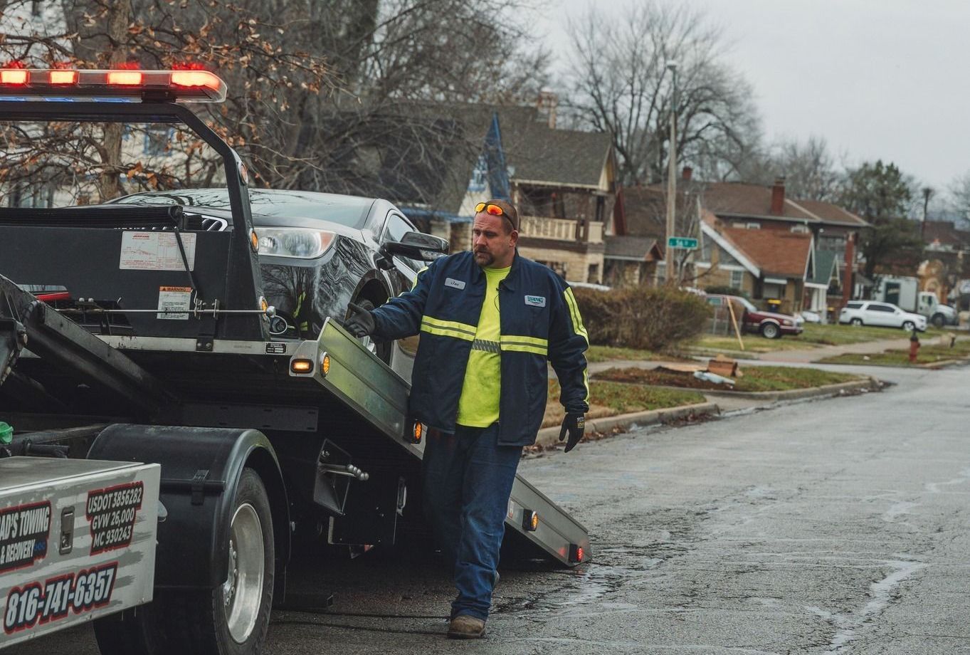 A man is standing next to a tow truck that is carrying a car.