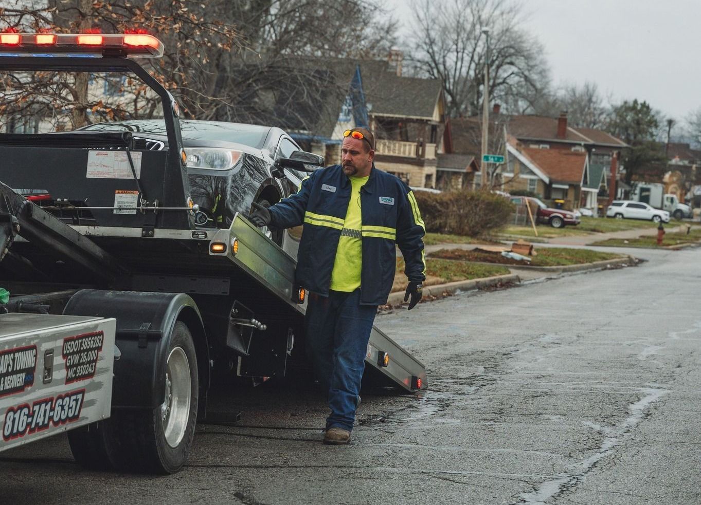 A man is walking towards a tow truck with a car on it.