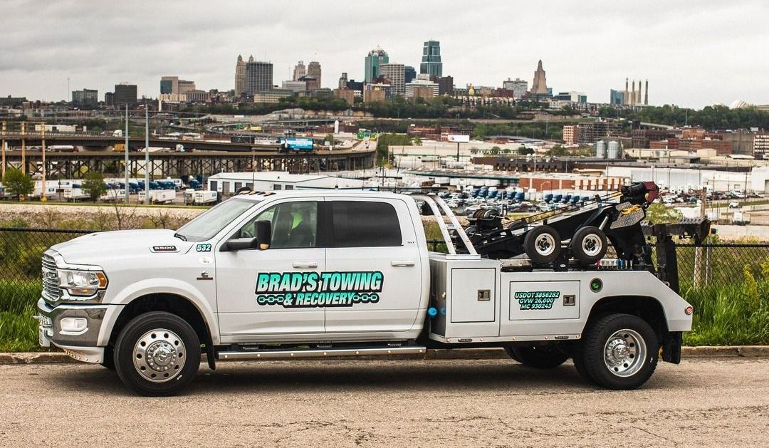 A white tow truck with a atv on the back is parked in front of a city.