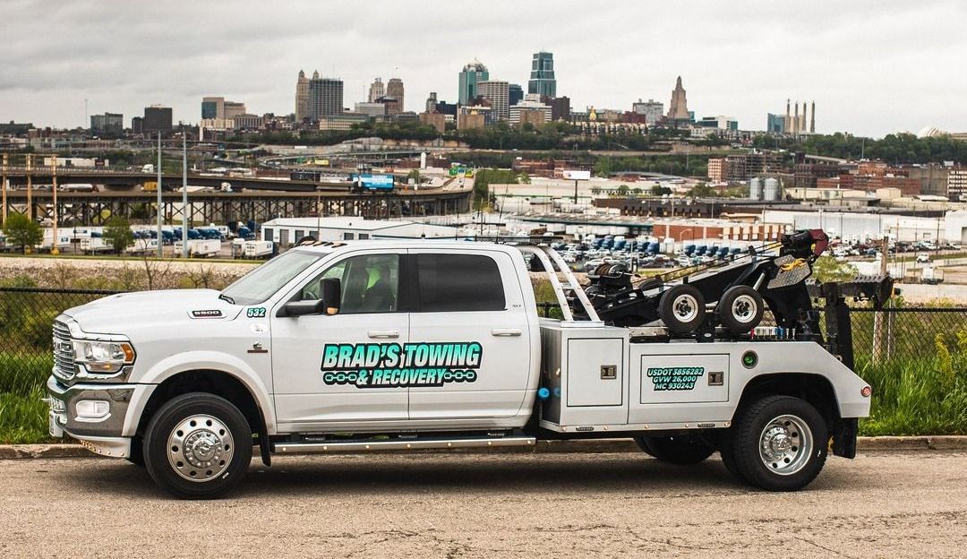 A white tow truck is parked on a gravel road in front of a city.
